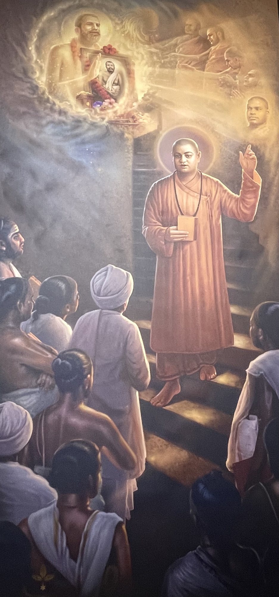 Painting of Swami Vivekananda in a saffron robe, standing on a staircase and addressing a gathering, with Sri Ramakrishna shown in a glowing aura at the top left.